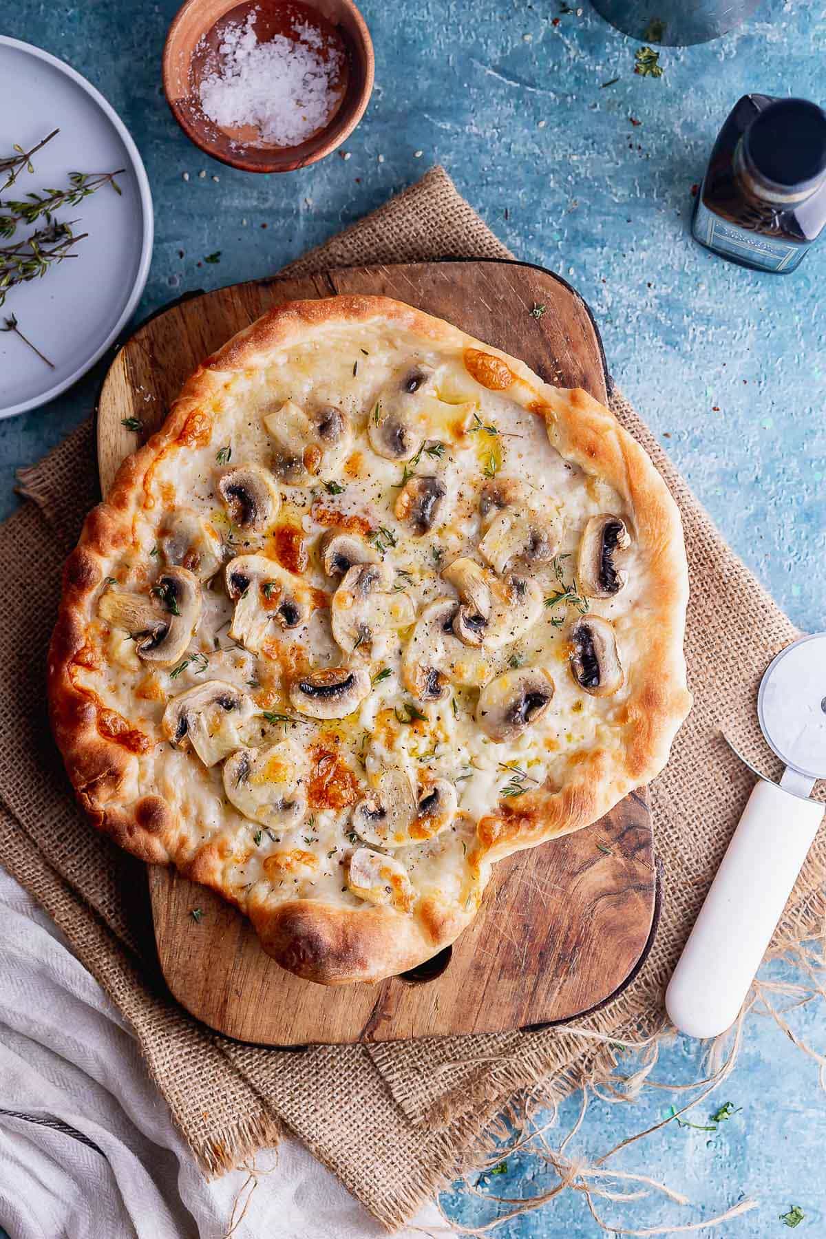 Overhead shot of pizza with mushrooms on a wooden board over a blue background