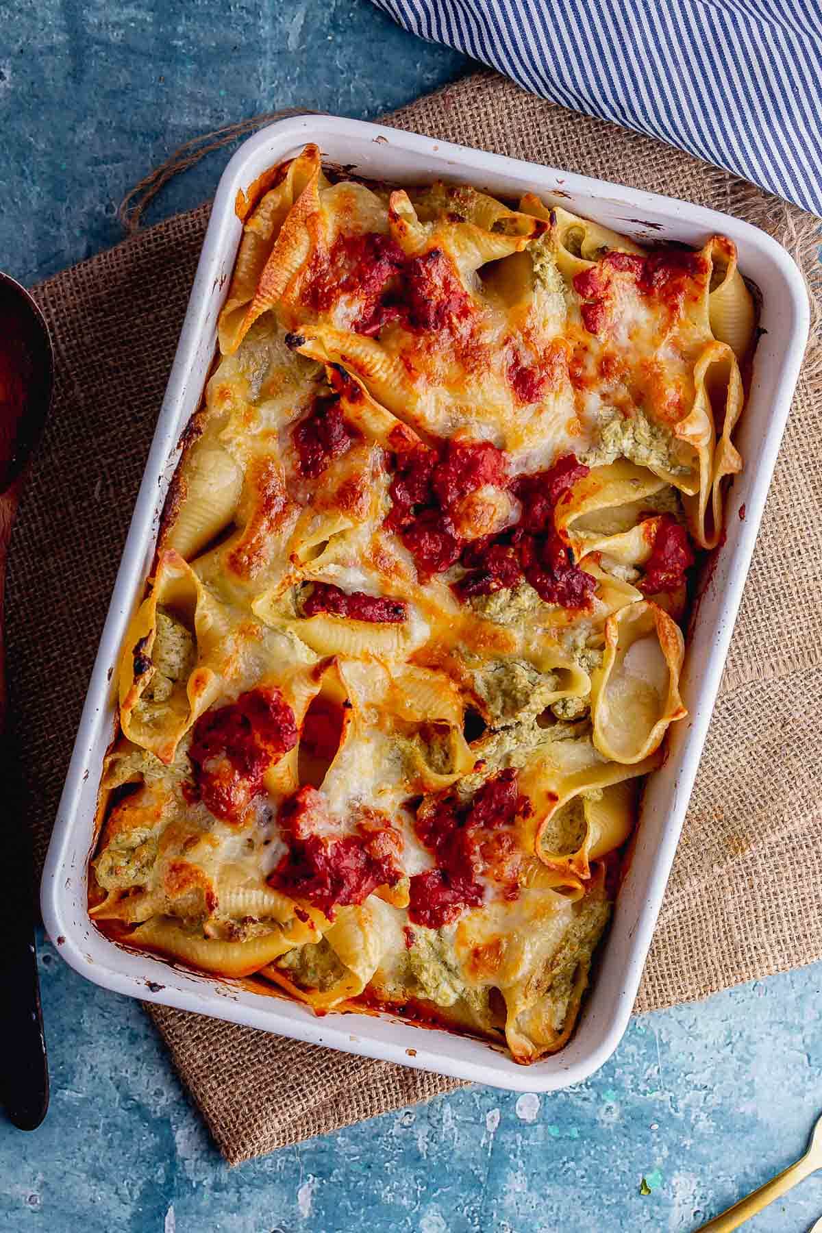 Overhead shot of pesto pasta bake in a baking dish on a blue background