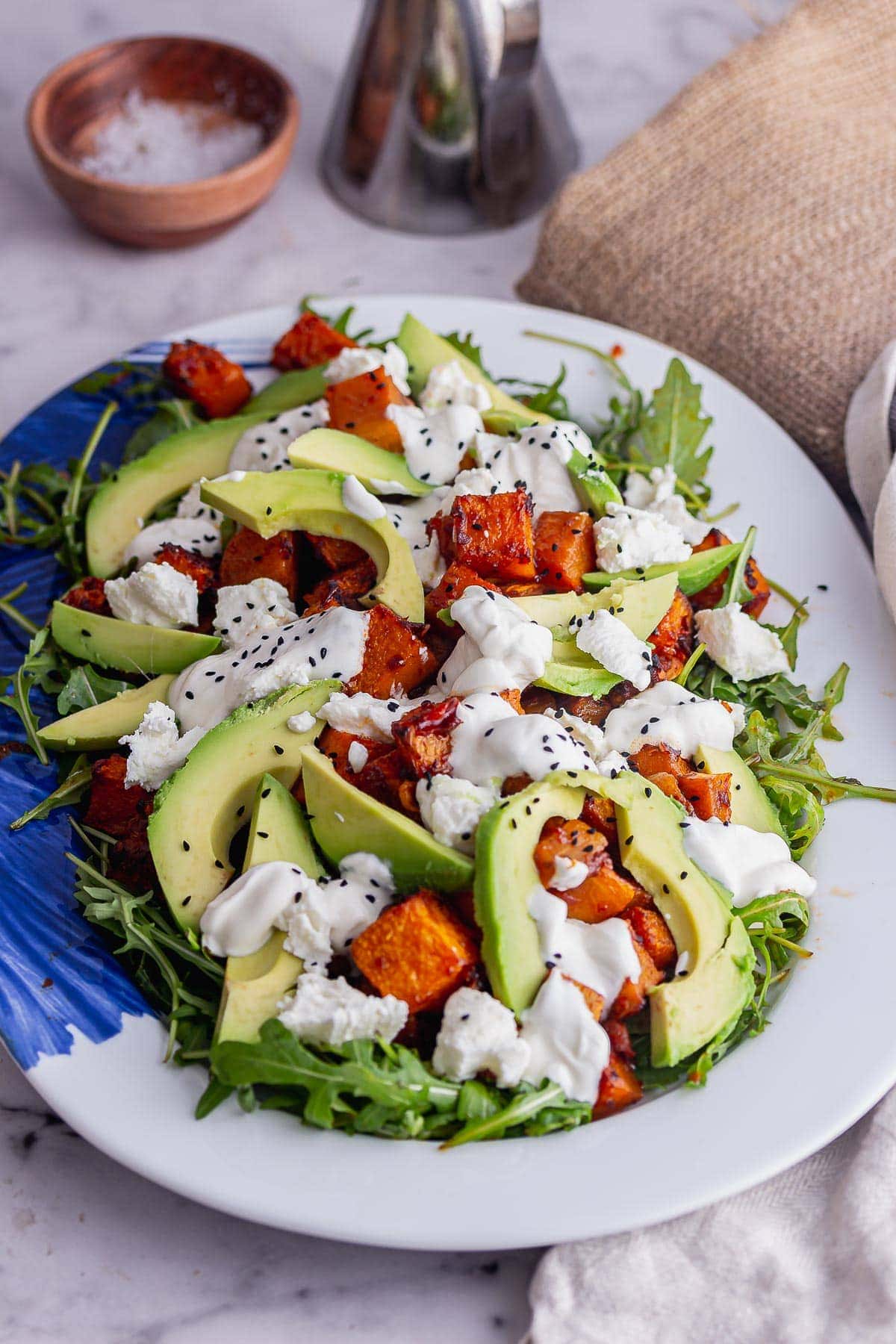 Plate of green salad with squash and avocado on a marble surface