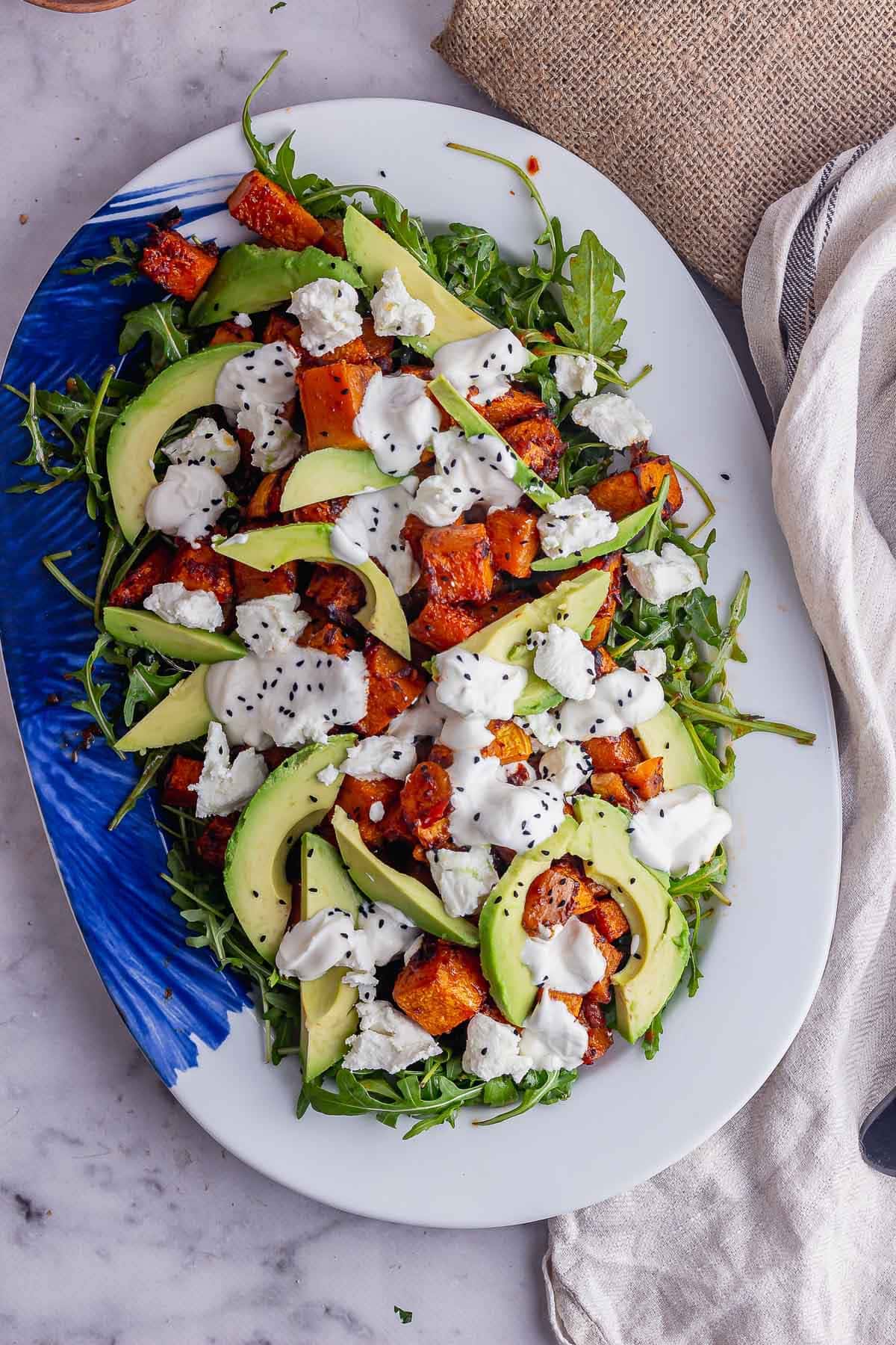 Overhead shot of butternut squash salad with avocado on a marble background