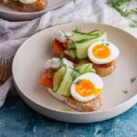 White bowl of smoked salmon toasts with egg and cucumber