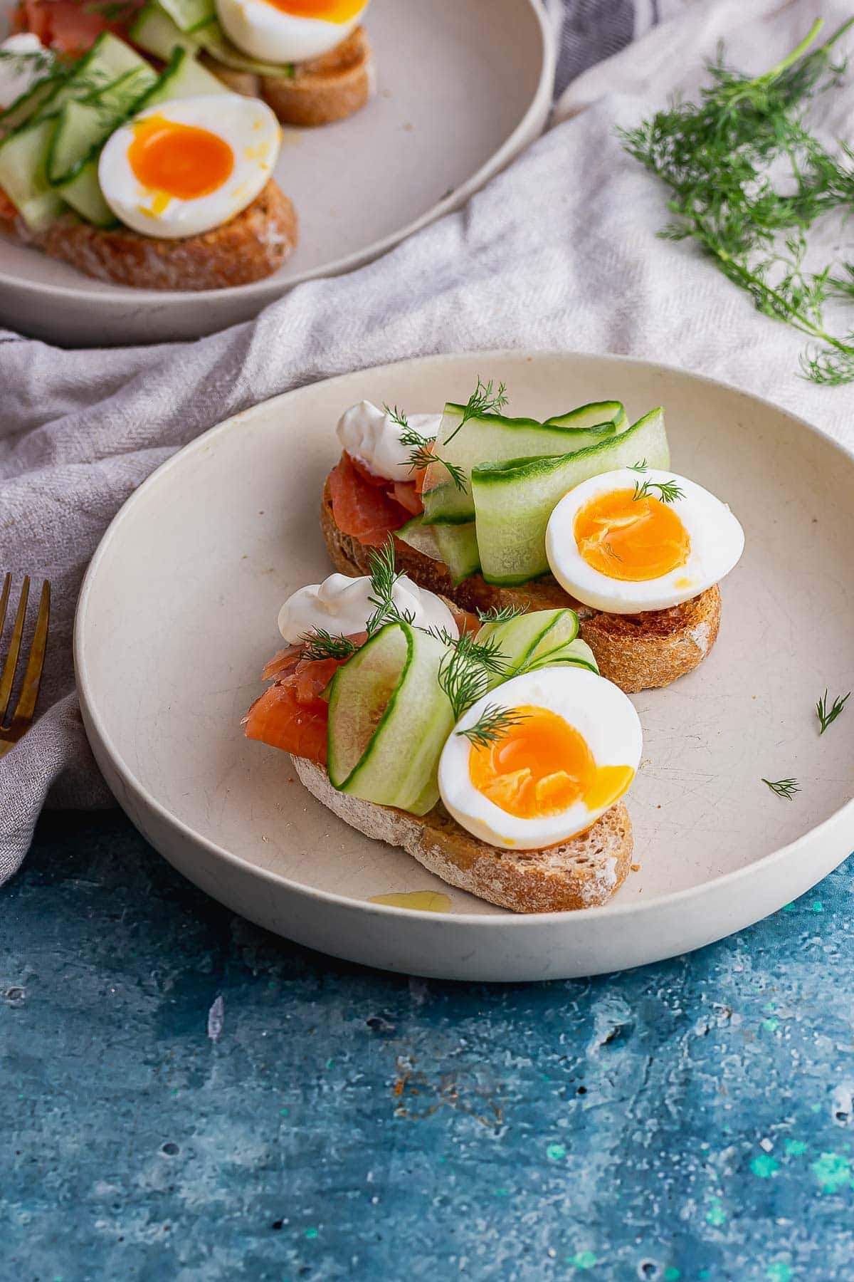 White bowl of smoked salmon toasts with egg and cucumber