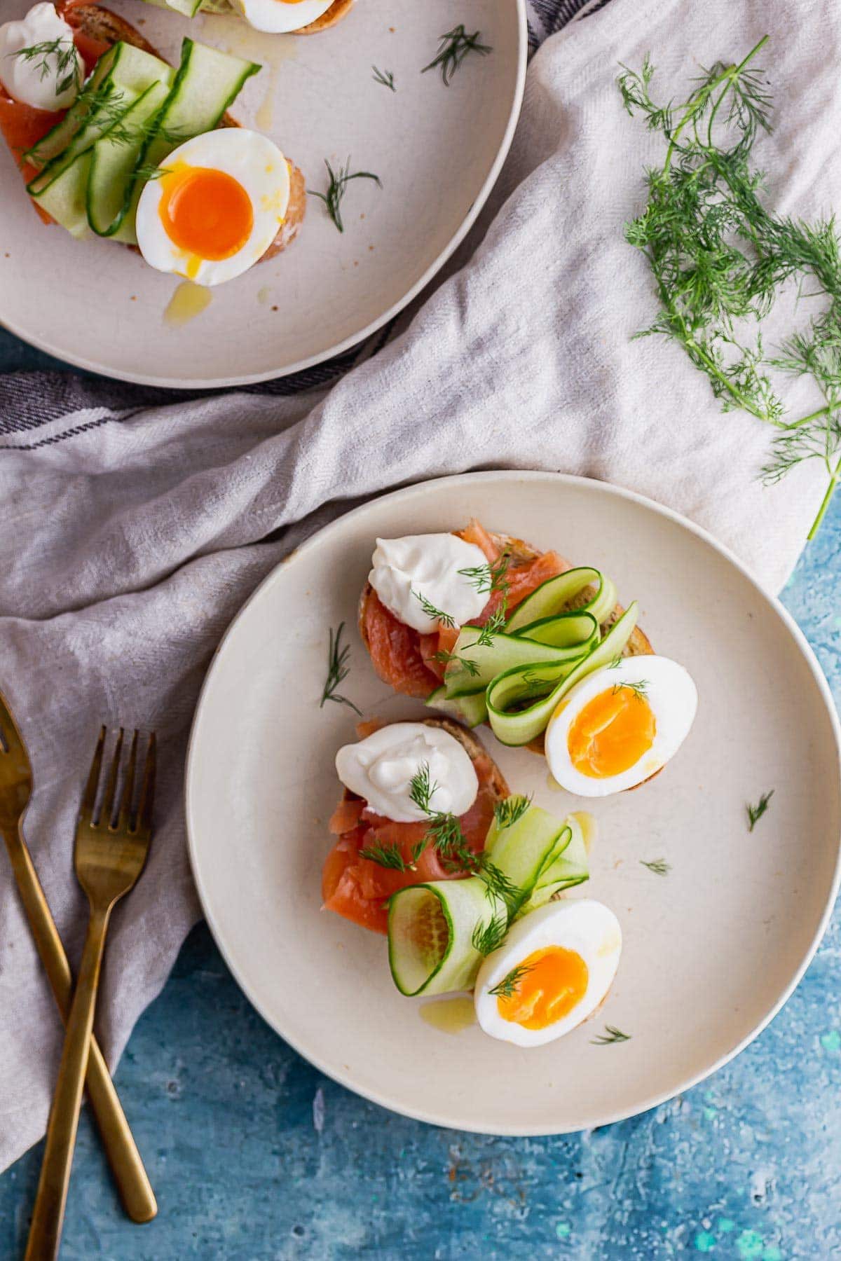 Overhead shot of plates of brunch toasts with smoked salmon and eggs on a blue background