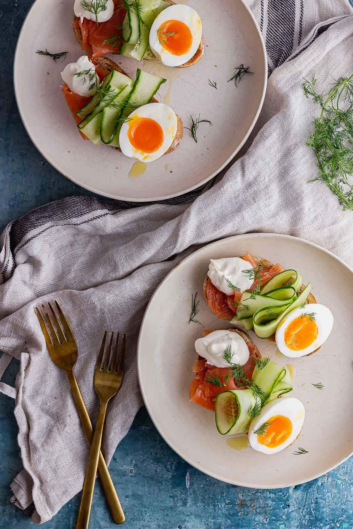 Overhead shot of plates of smoked salmon breakfast toasts with gold cutlery