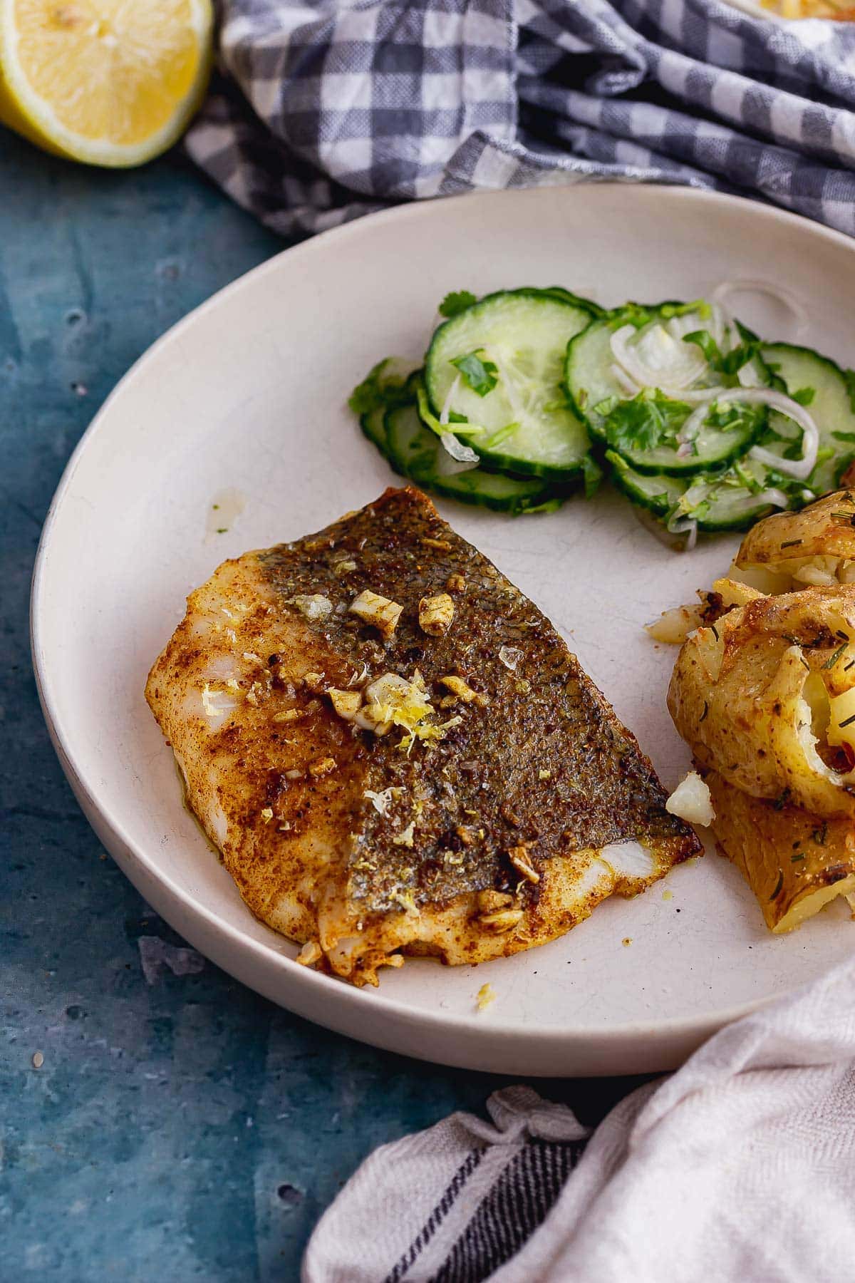 Spiced fish on a white plate with cucumber salad