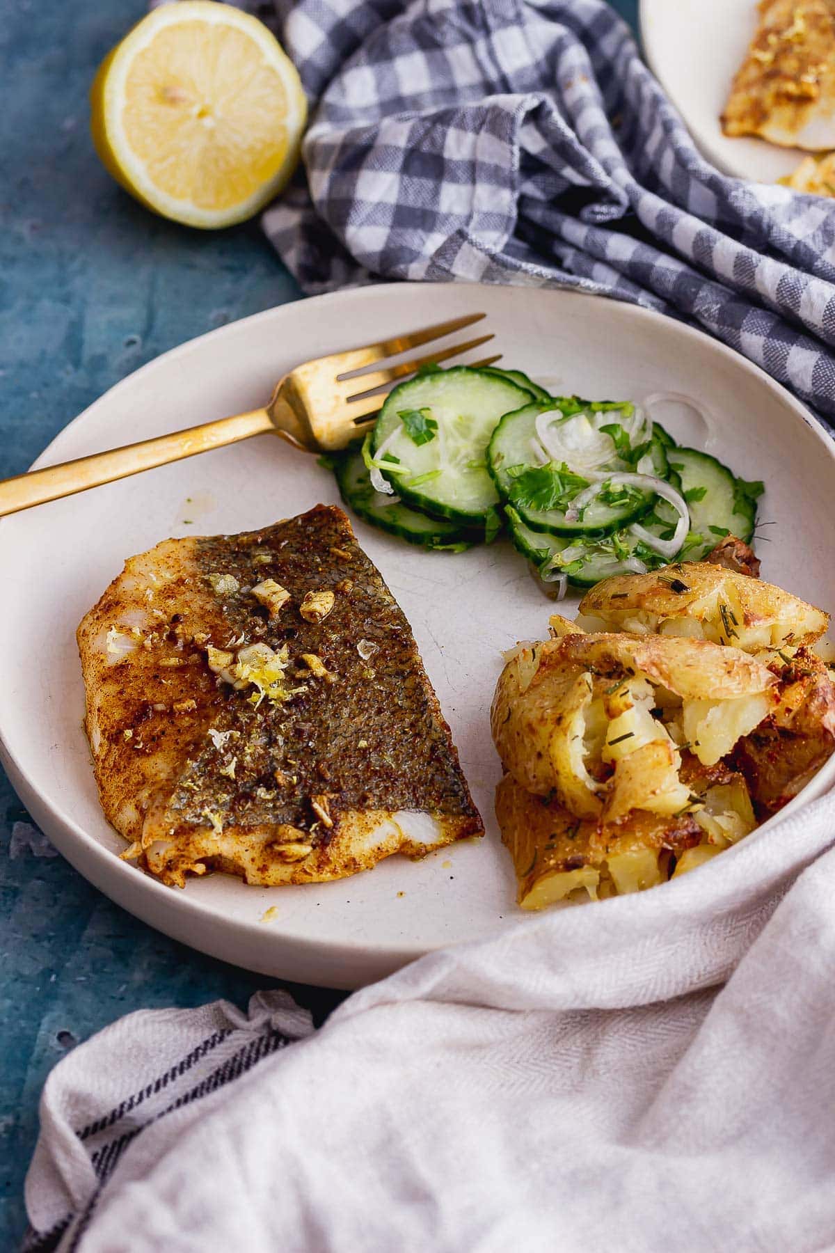 Fish, potatoes and cucumber in a white bowl with a checked cloth