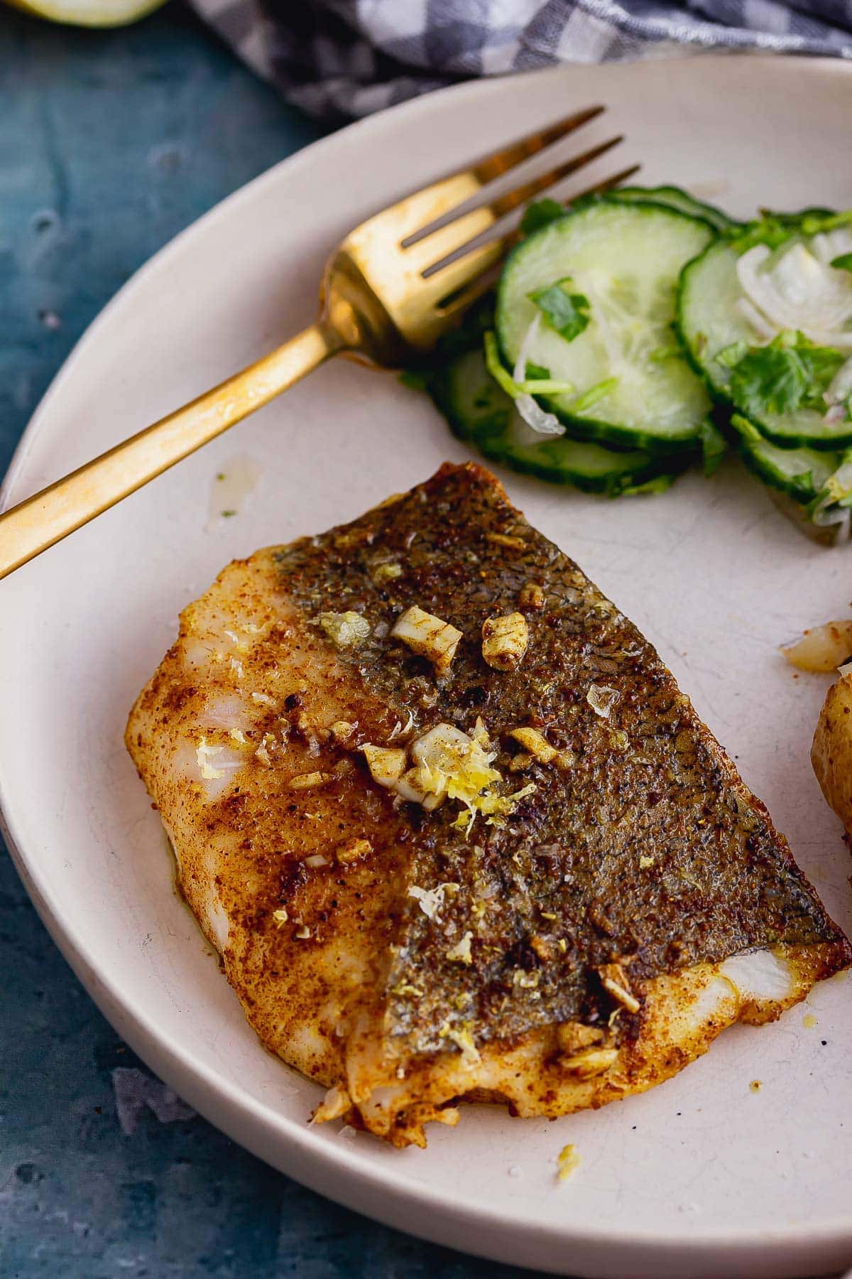 Baked fish fillet in a white bowl with cucumber