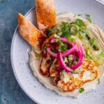 Overhead shot of halloumi aubergine hummus bowl with bread in a blue bowl