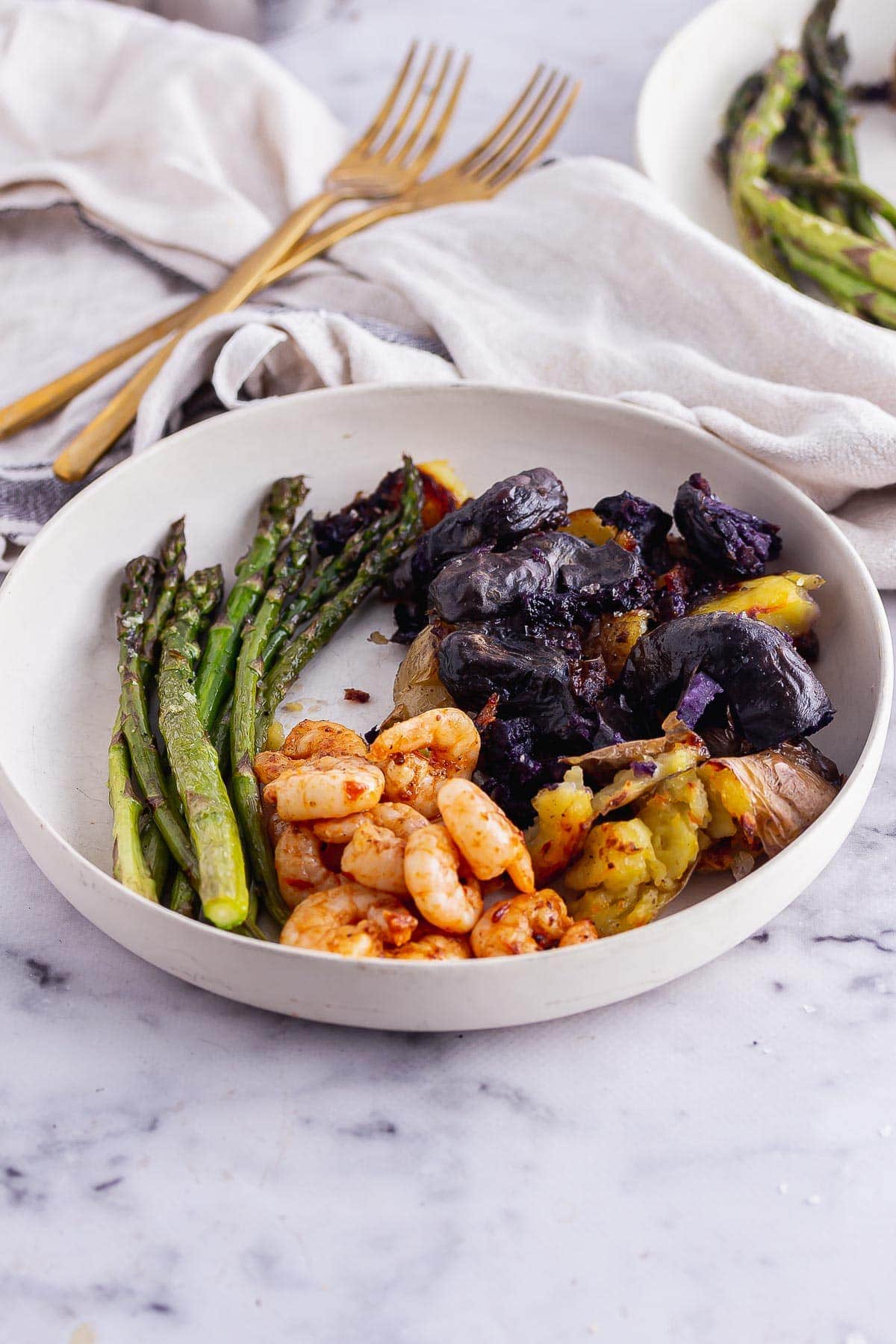 White bowl of harissa prawns with asparagus and potatoes