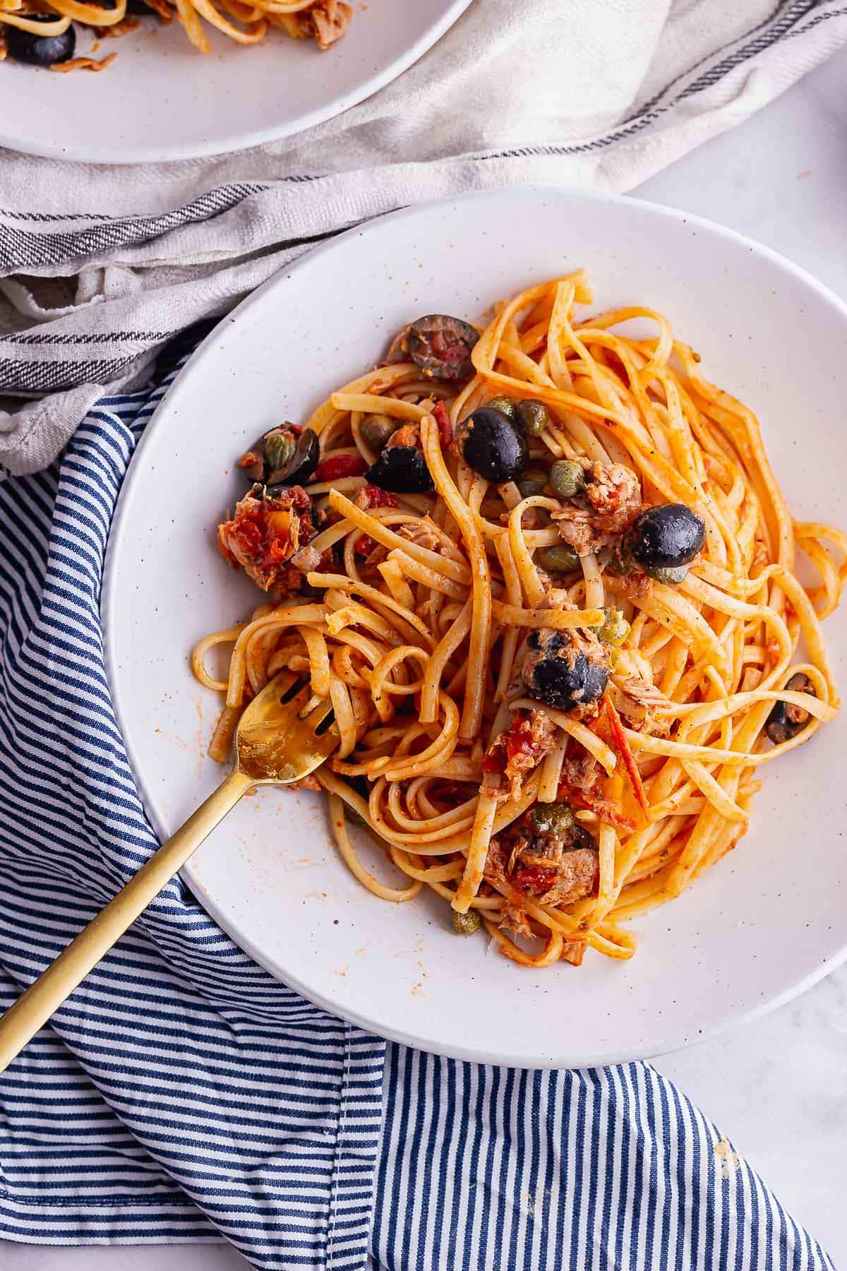 Spaghetti puttanesca flat lay with a gold fork on a striped cloth