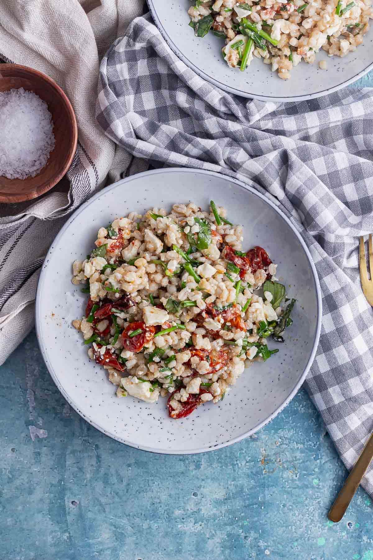 Flat lay shot of a bowl of pearl barley salad with a checked cloth on a blue background
