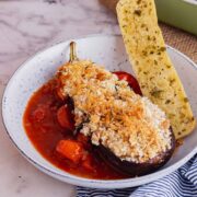 Blue bowl of cheesy aubergine with tomato sauce and garlic bread on a marble background