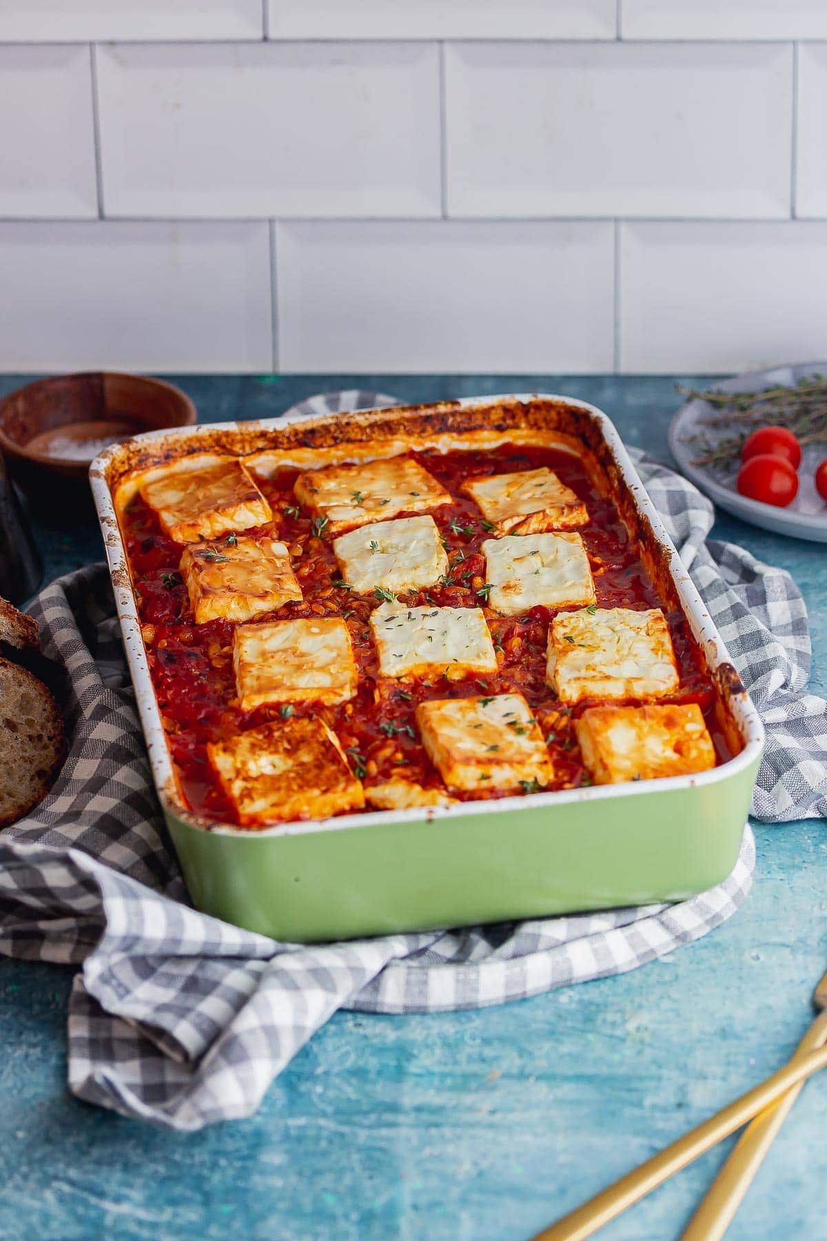 Green baking dish of baked lentils topped with feta on a blue surface