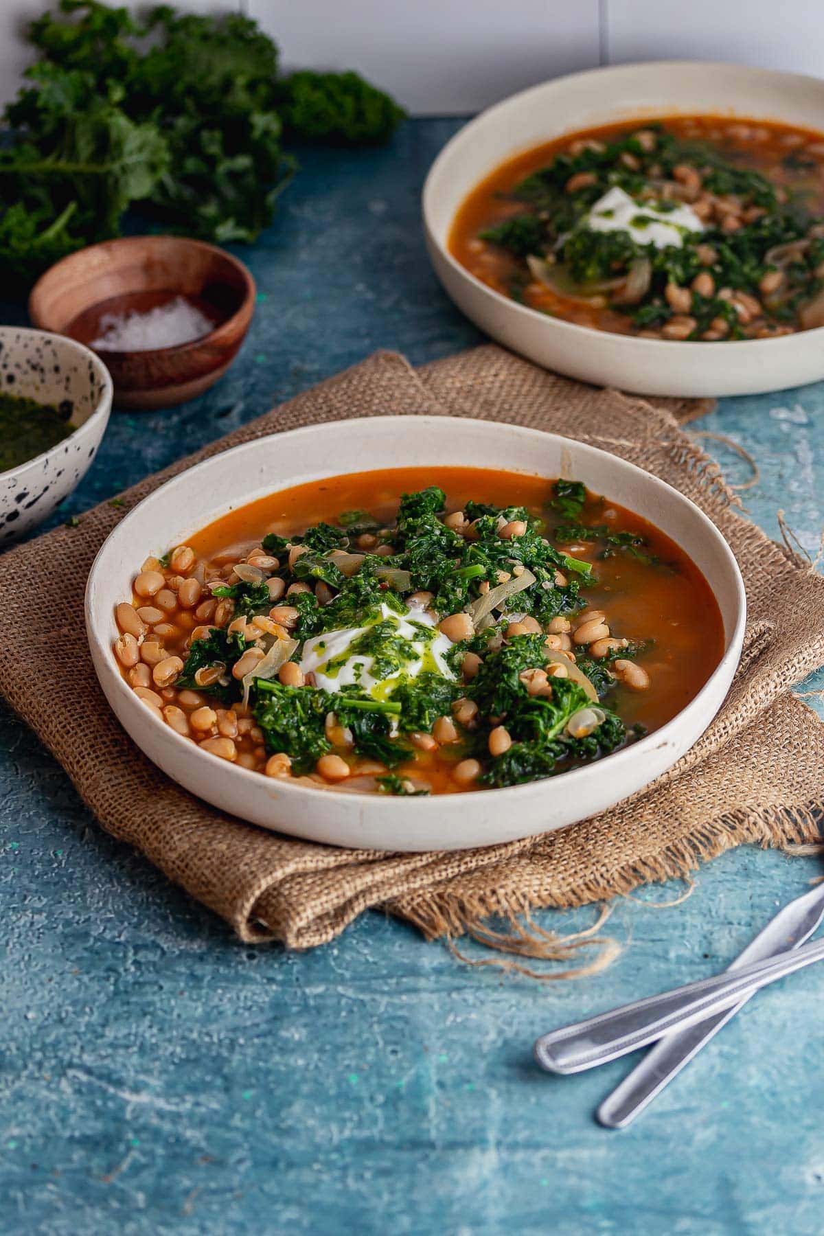 Bowl of harissa soup with beans topped with herbs on a hessian mat