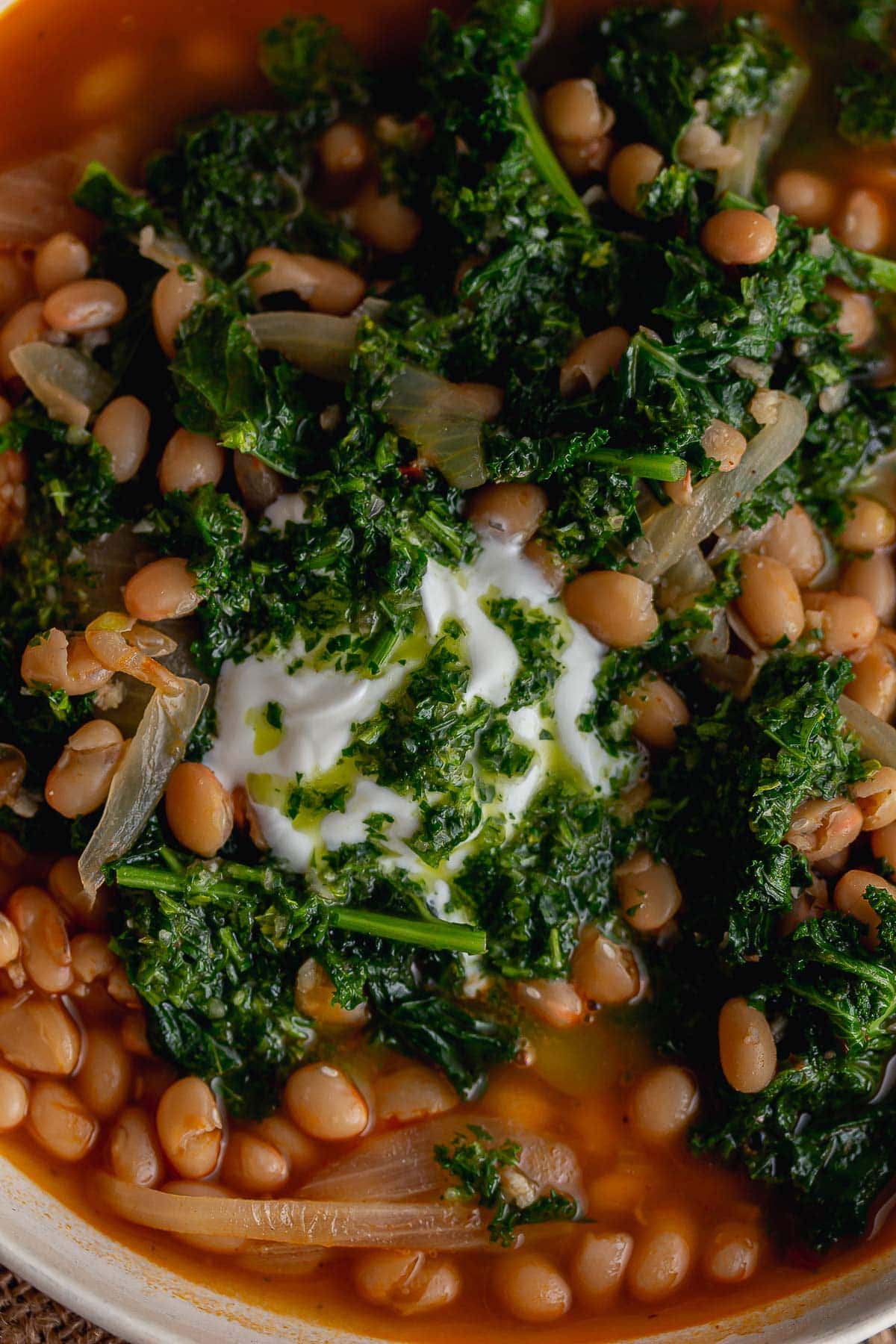 Close up of beans and kale in a soup topped with yoghurt
