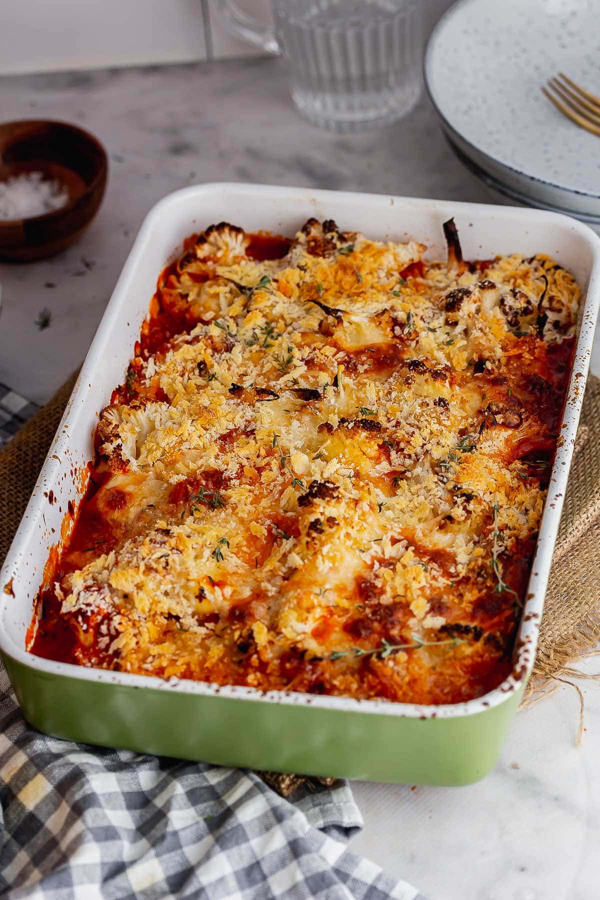 Green baking dish of cheese and tomato baked cauliflower on a marble surface