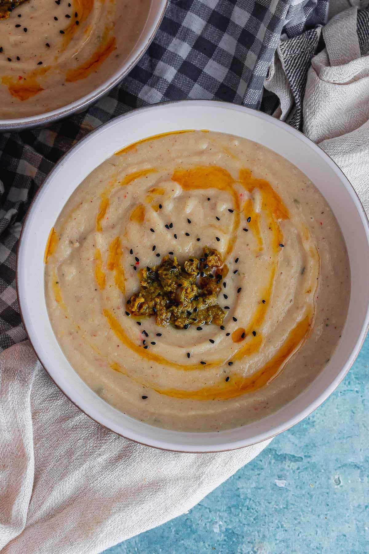 Overhead shot of roasted cauliflower soup drizzled with chilli oil on a blue background