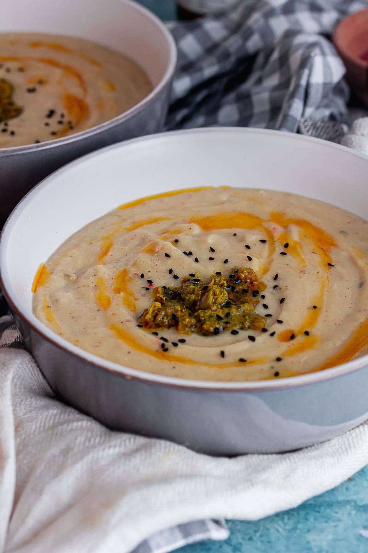 Grey bowl of cauliflower soup topped with nigella seeds on a cloth