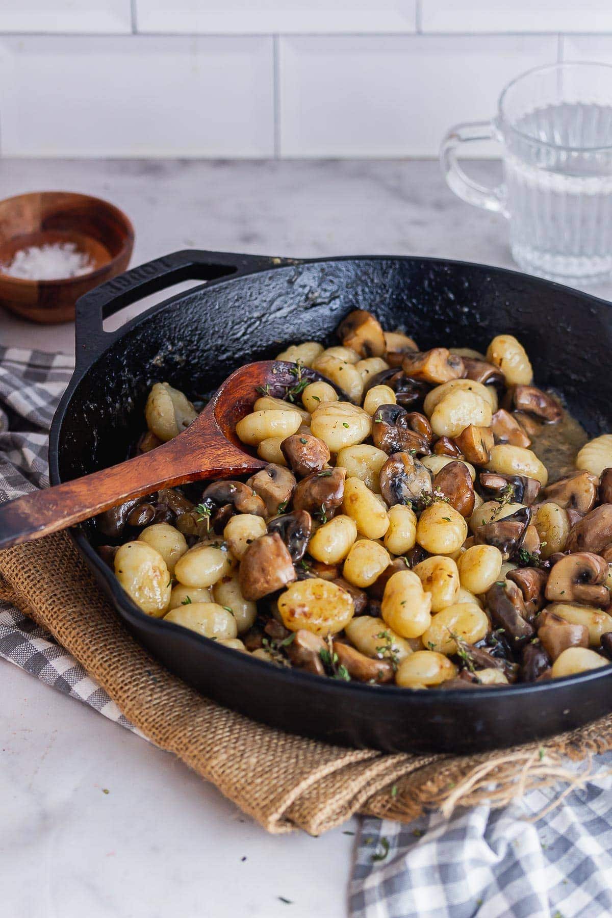 Black skillet of mushroom gnocchi with a wooden spoon on a marble background