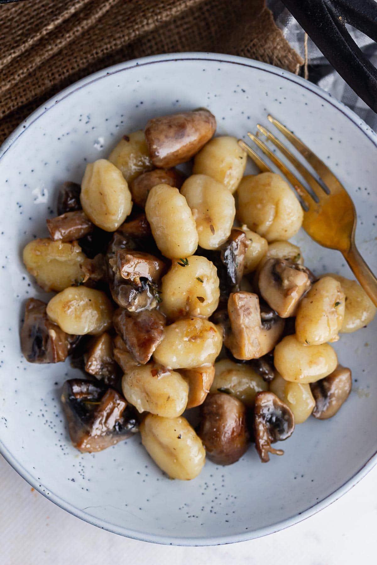 Overhead shot of gnocchi and mushrooms in a blue bowl with a gold fork