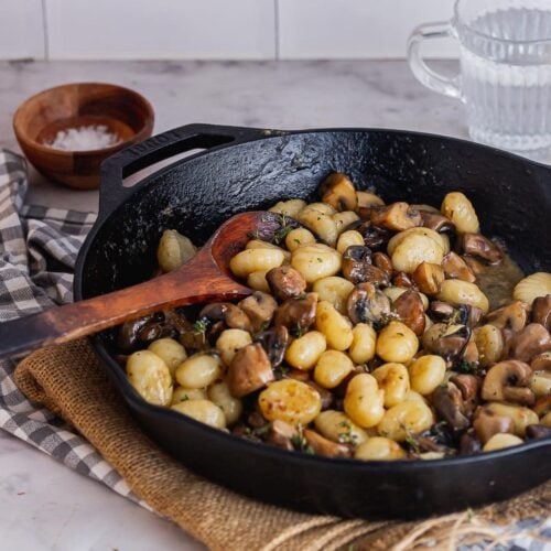Black skillet of gnocchi with mushrooms on a marble background
