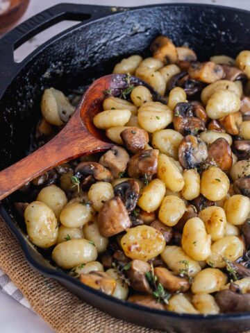 Gnocchi in a cast iron skillet with a wooden spoon on a hessian mat