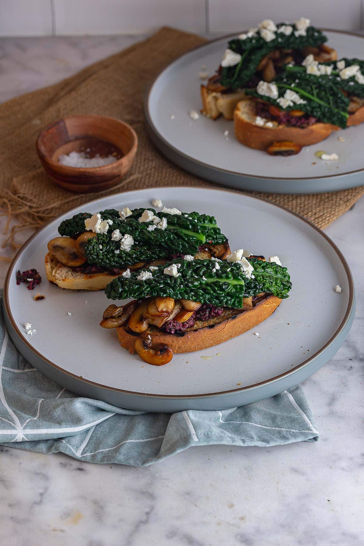 Grey plate of toasts topped with mushrooms and cavolo nero on a blue cloth