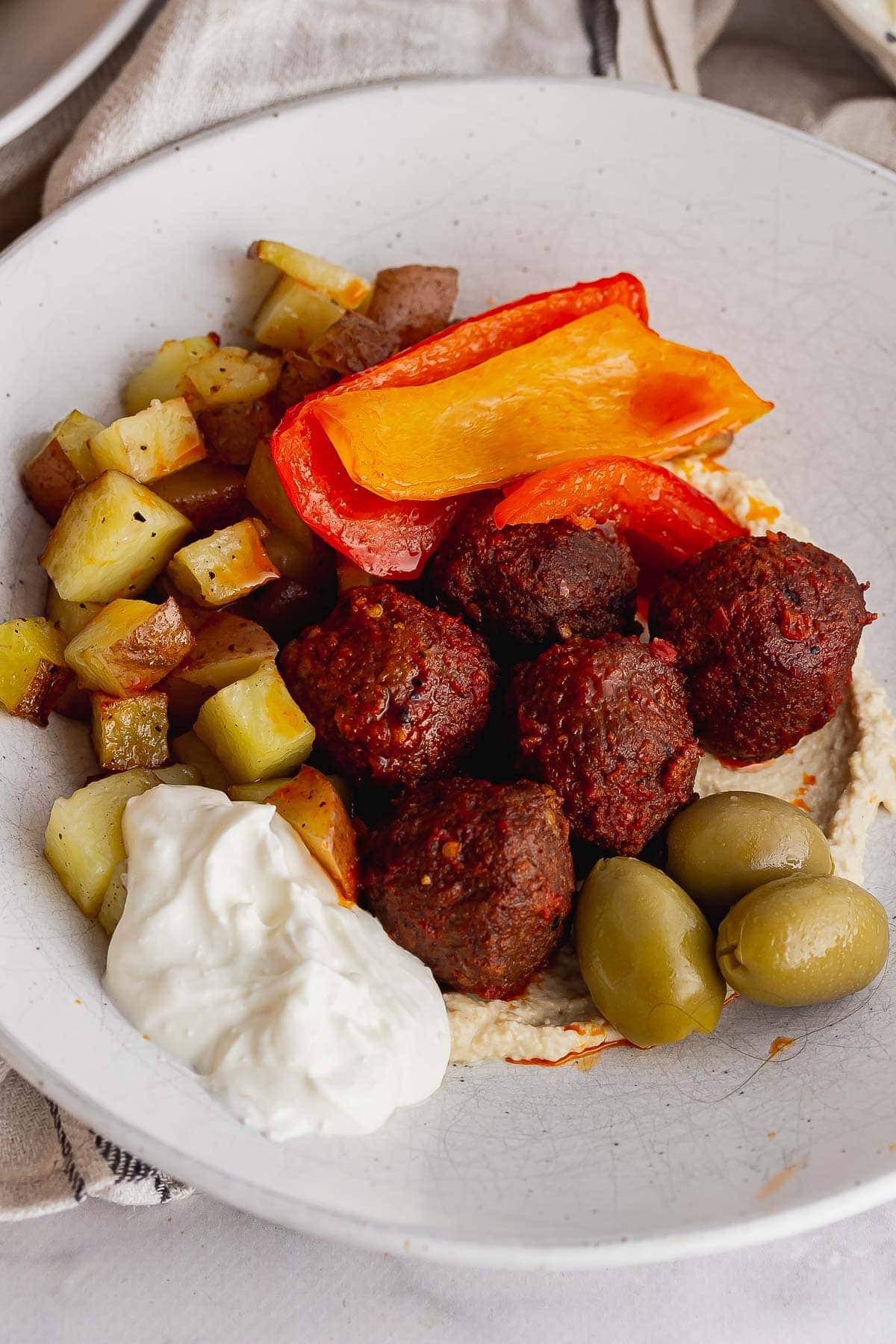 Close up of spicy meatballs, potatoes and peppers on hummus