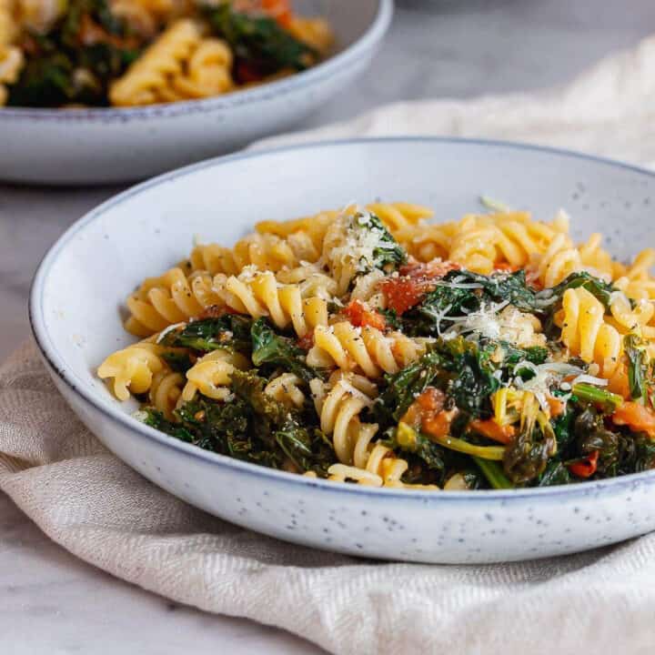 Blue bowl of pasta with tomatoes and kale