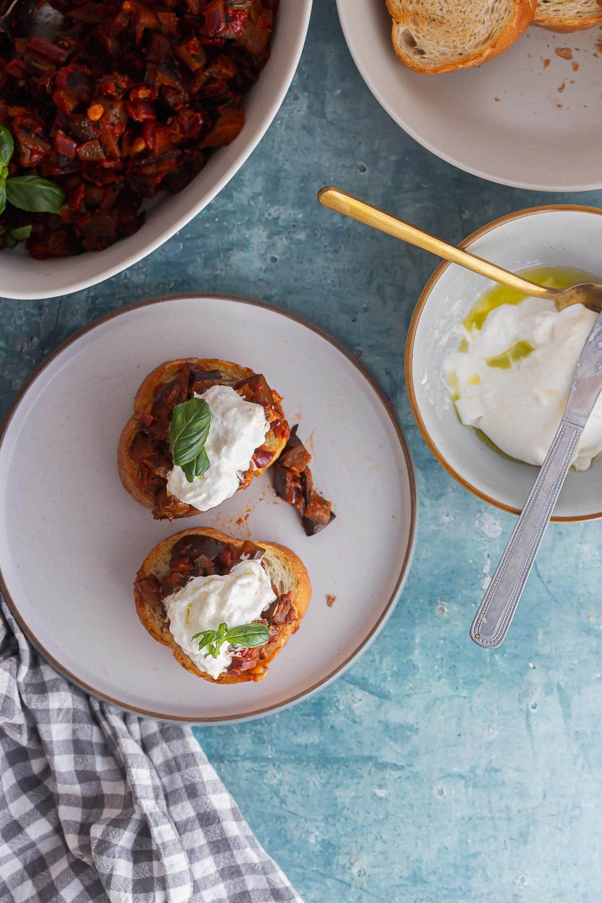 Overhead shot of caponata toasts topped with burrata on a blue background