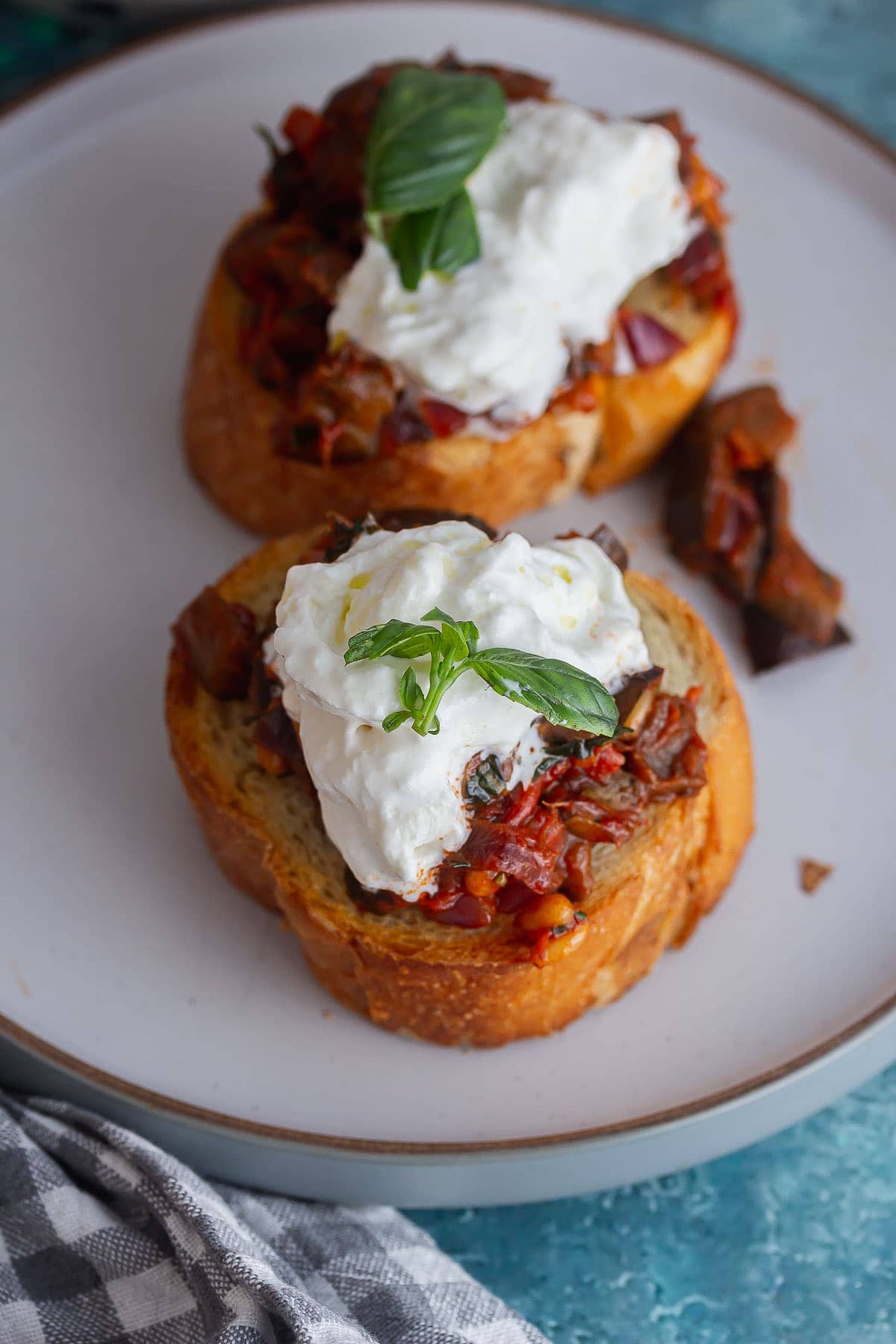 Two toasts topped with aubergine and cheese on a grey plate