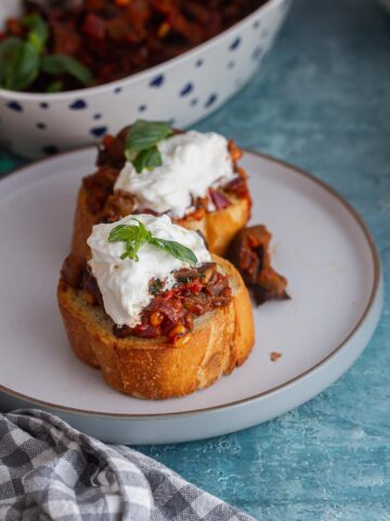 Grey plate of caponata toasts topped with burrata