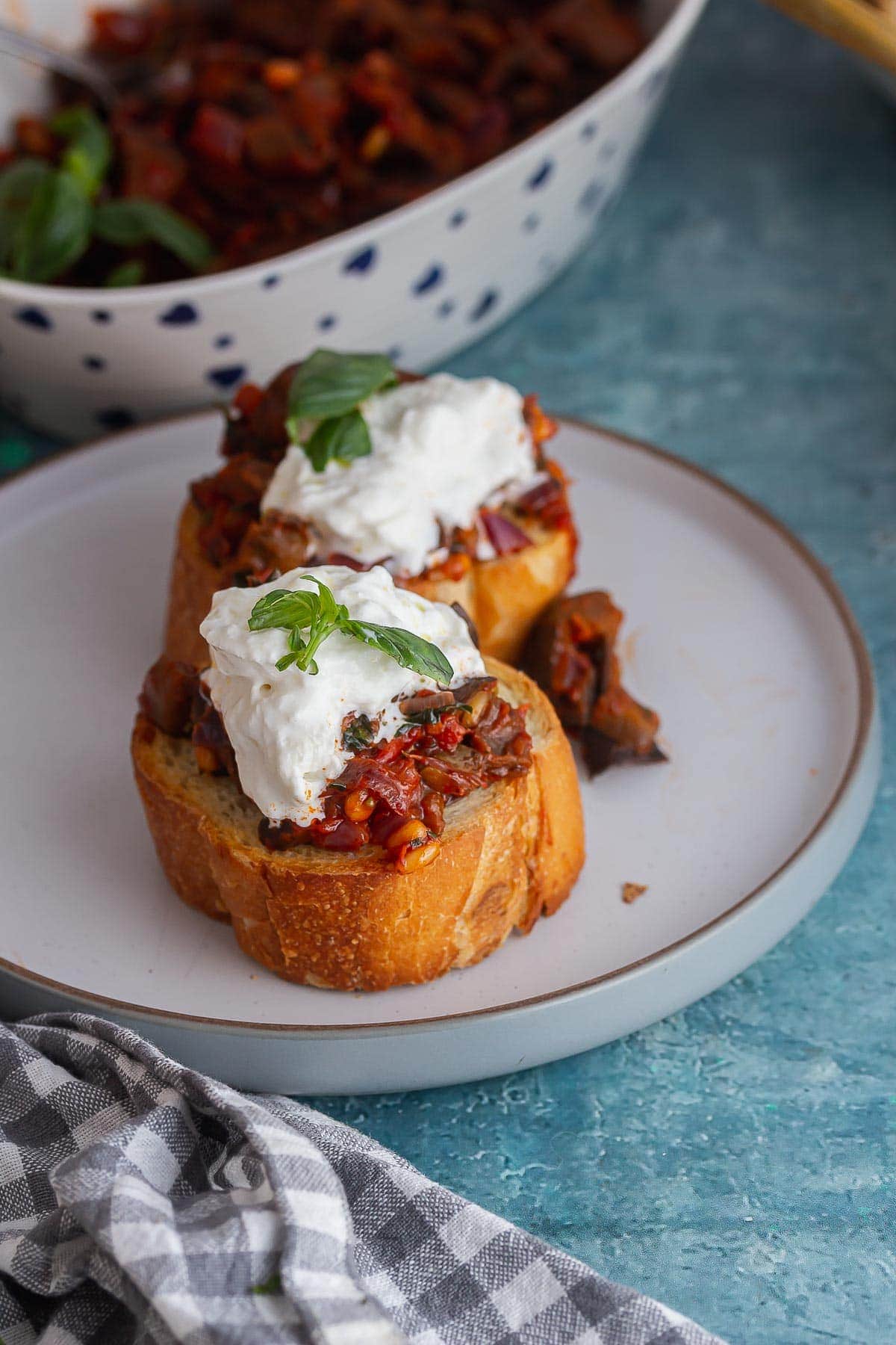 Grey plate of caponata toasts topped with burrata