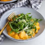 Blue bowl of butternut squash gnocchi with a gold fork