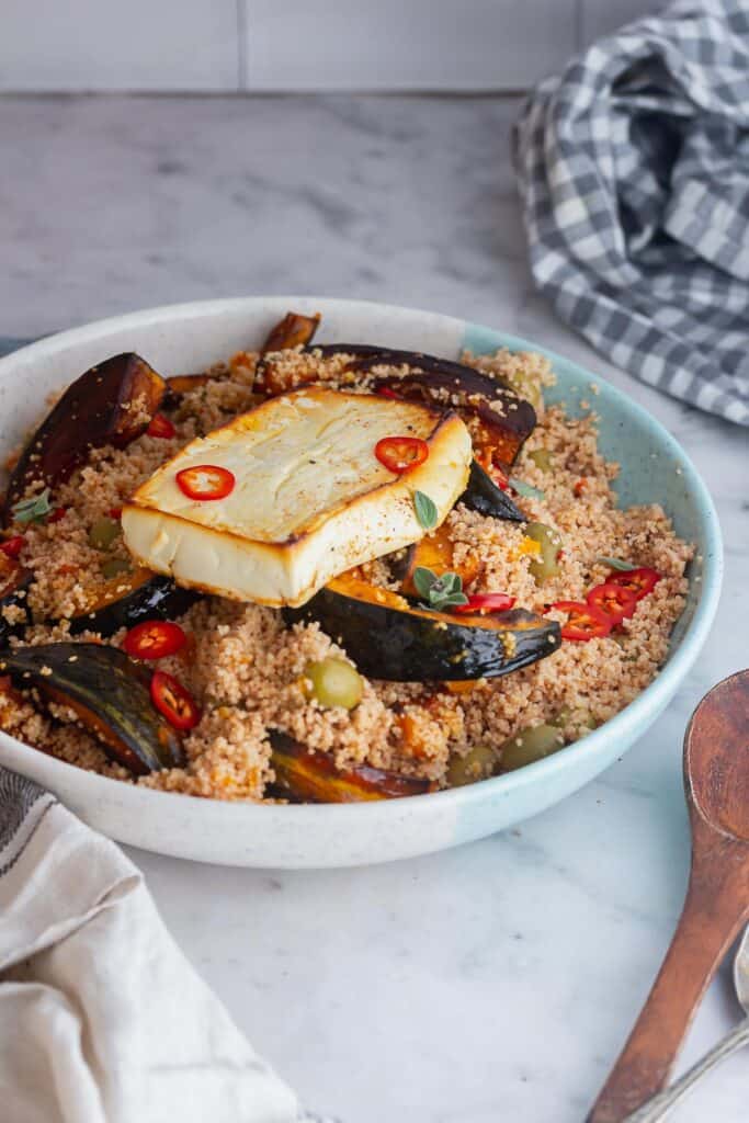 Bowl of couscous salad topped with feta on a marble background