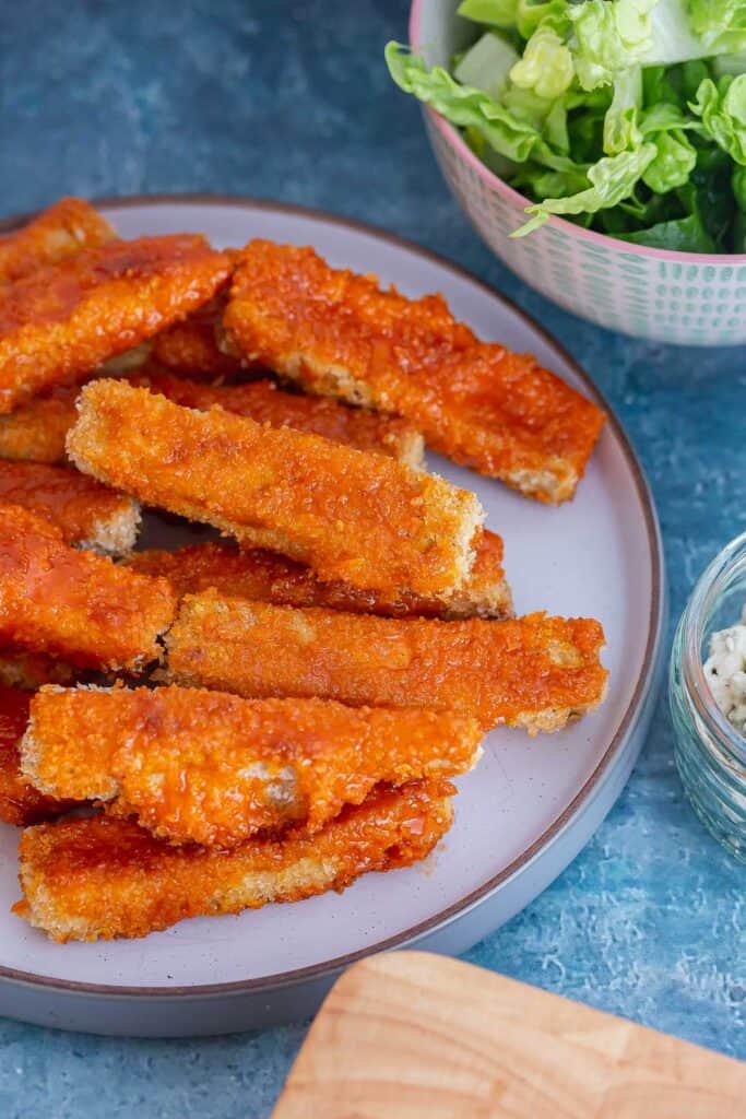 Plate of tofu coated in buffalo sauce on a blue background