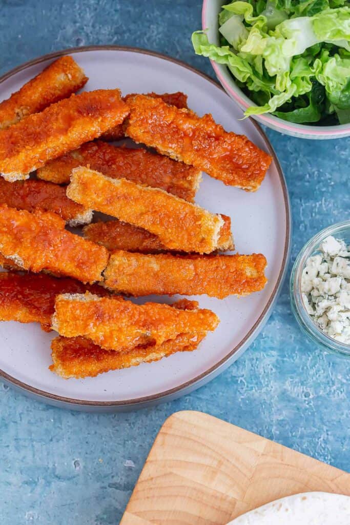 Plate of crispy tofu with bowls of lettuce and cheese all on a blue background