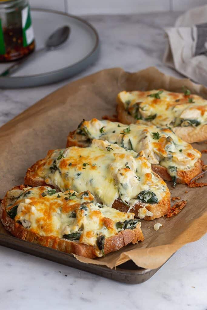 Toasts topping with spinach and artichoke on baking parchment on a baking sheet