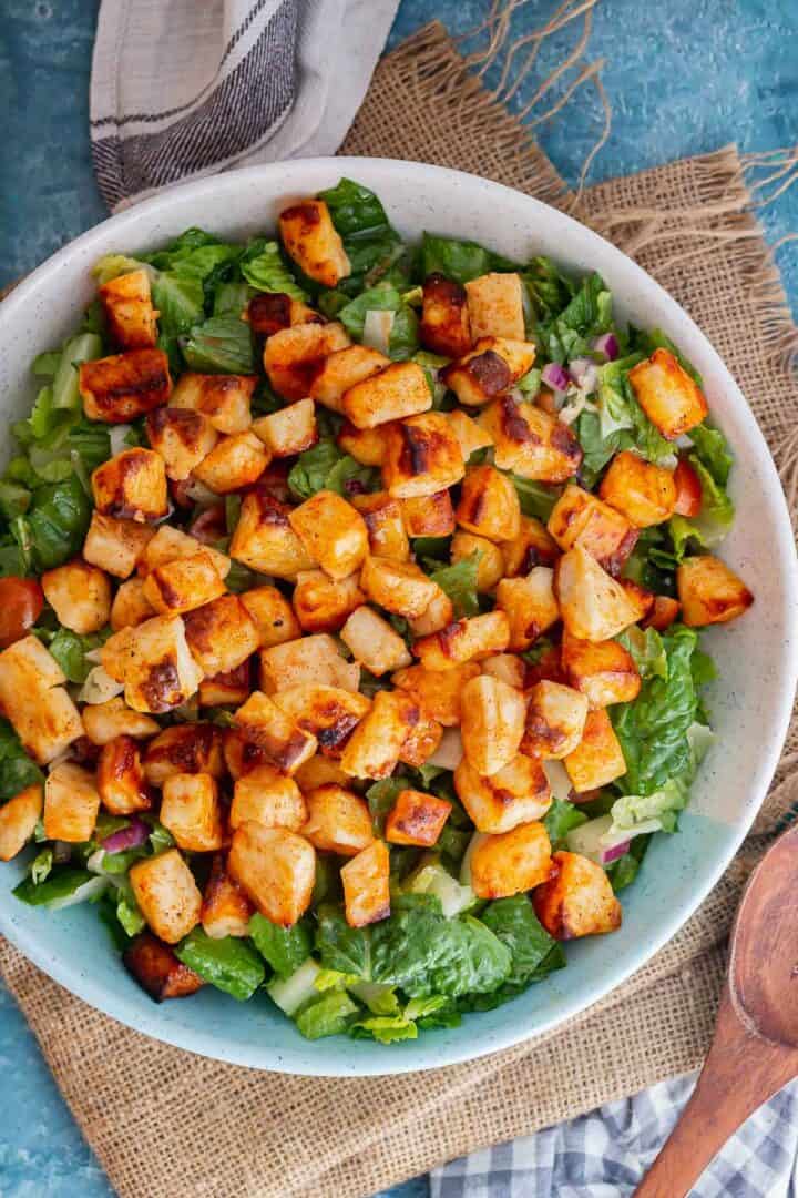 Overhead shot of halloumi on top of salad on a blue surface