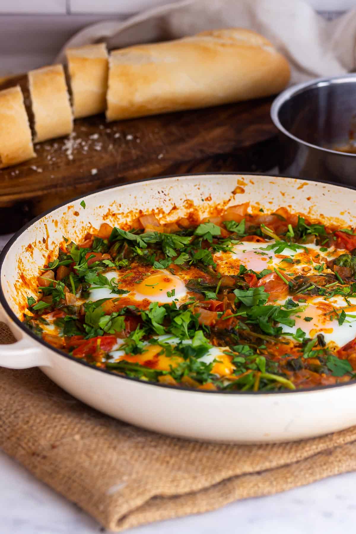 White pan of eggs in tomato sauce with herbs