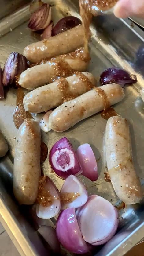Silver baking sheet of sausages and onion with honey mustard