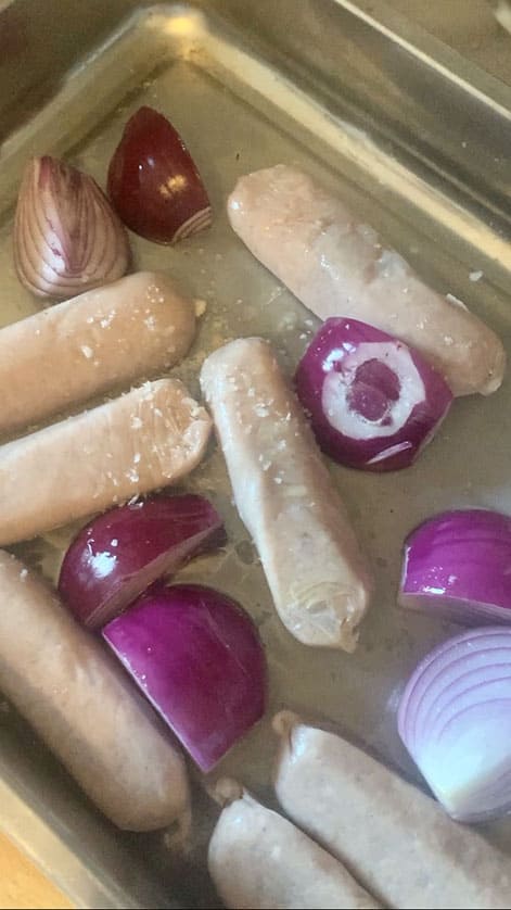 Silver baking sheet with red onions and sausages