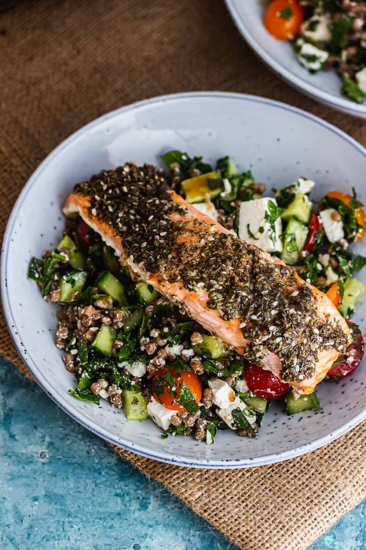 Blue bowl of salmon and couscous salad on a mat
