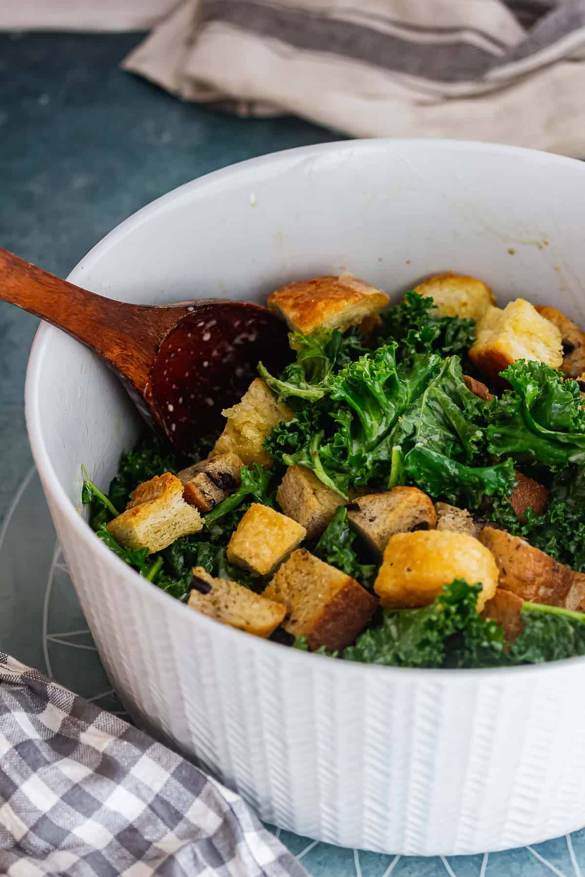 Grey bowl of kale salad with a wooden spoon