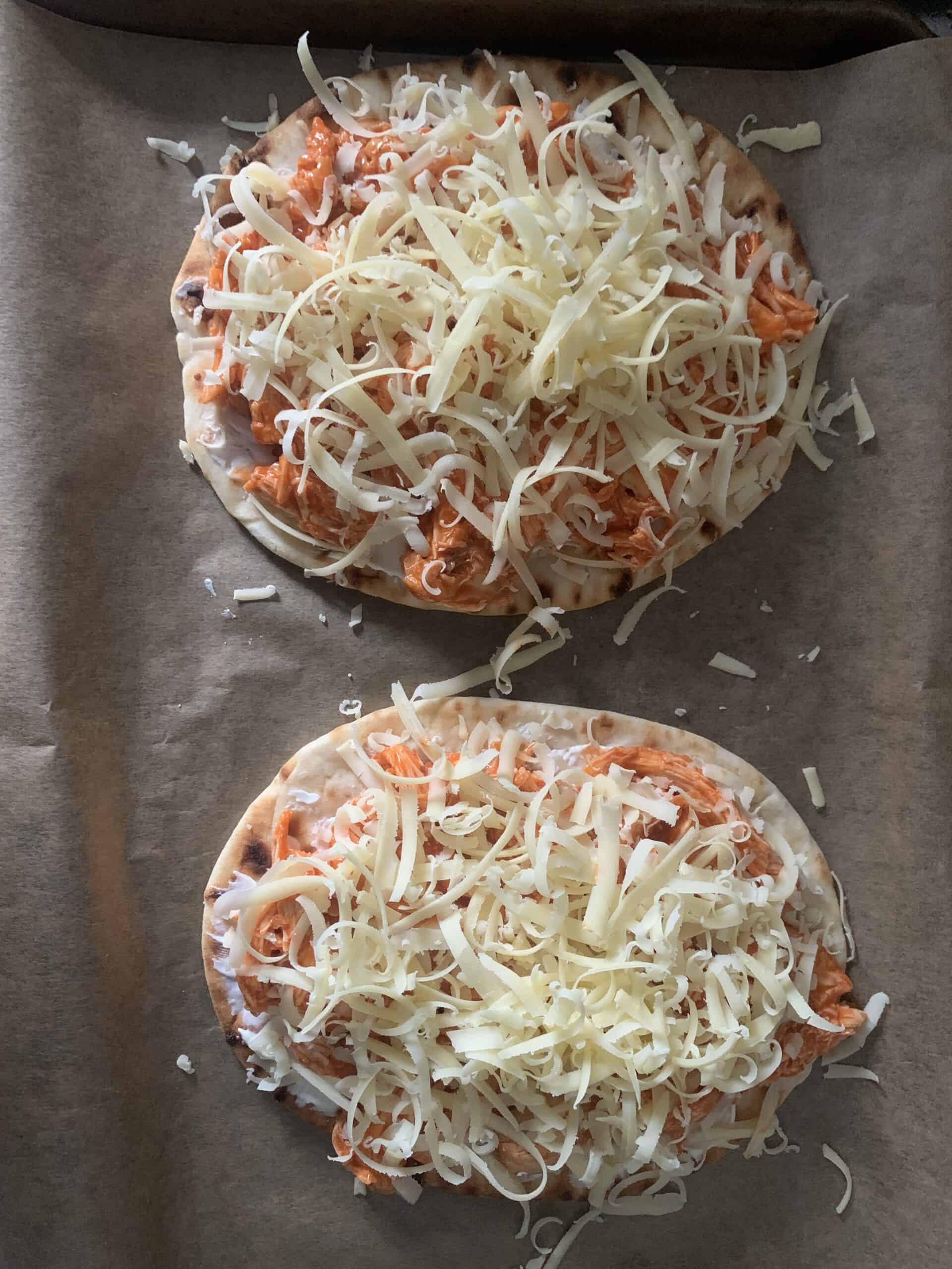 Two flatbread with chicken and grated cheese
