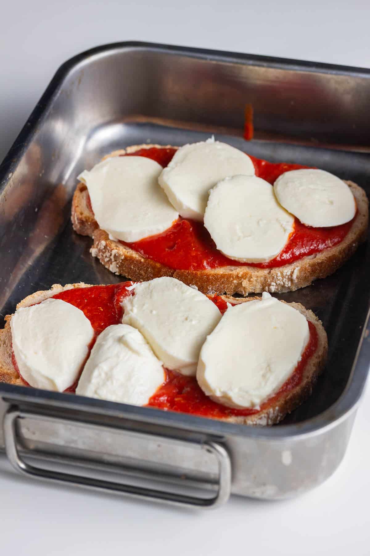 Silver tray of toast topped with sauce and mozzarella