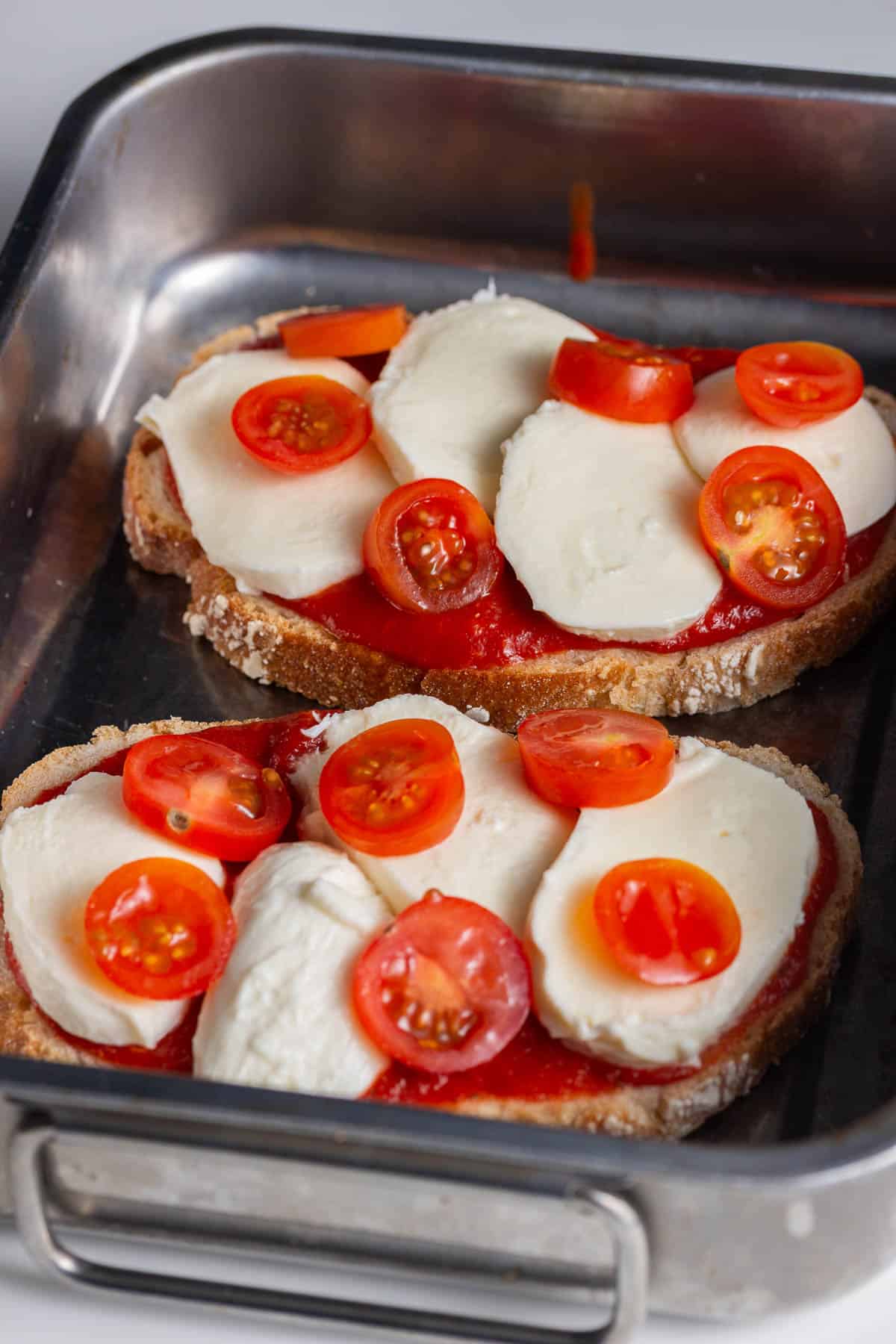 Silver tray of toasts topped with sauce, mozzarella and cherry tomatoes