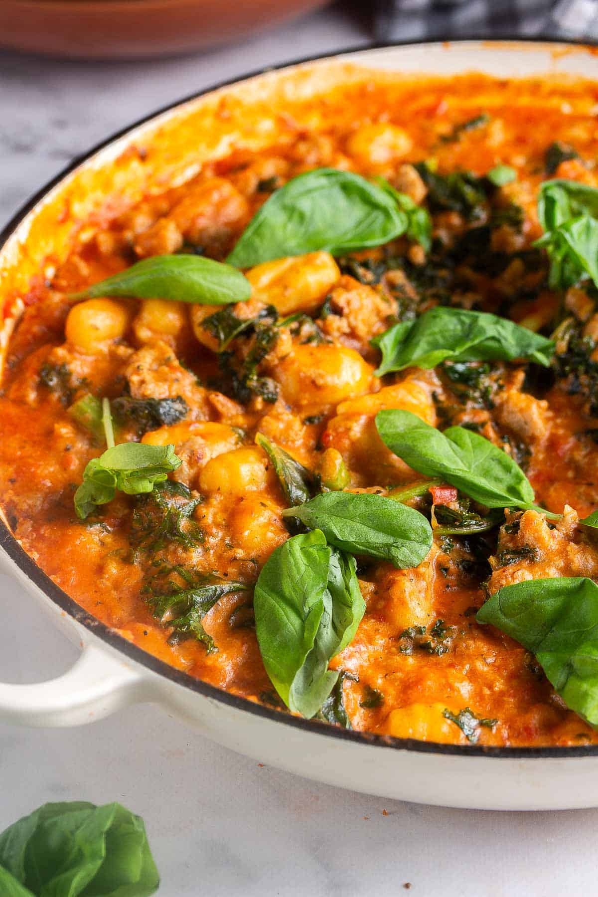 Skillet of gnocchi in sauce topped with basil