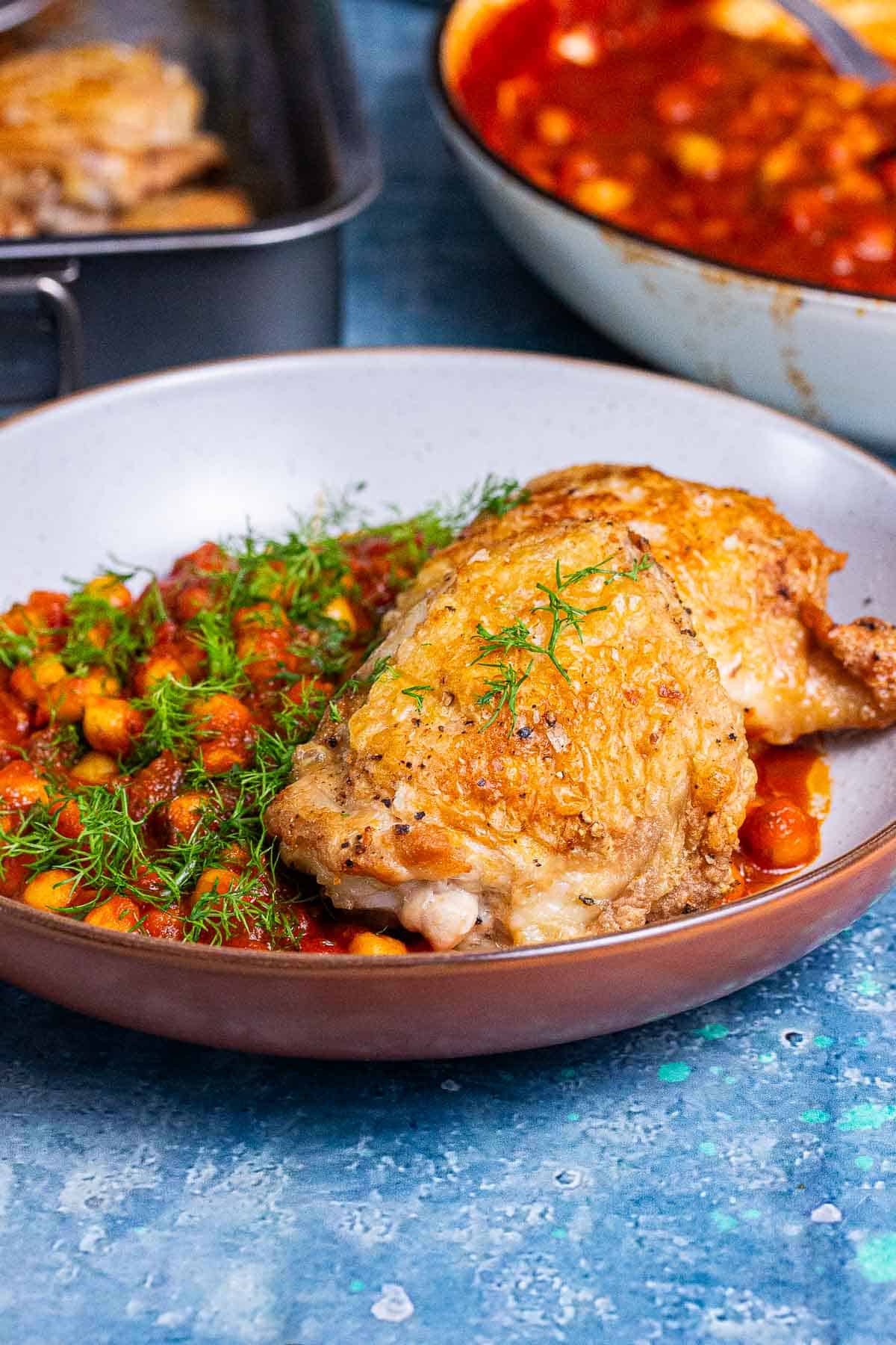 Bowl of crispy chicken thighs and stew on a blue surface